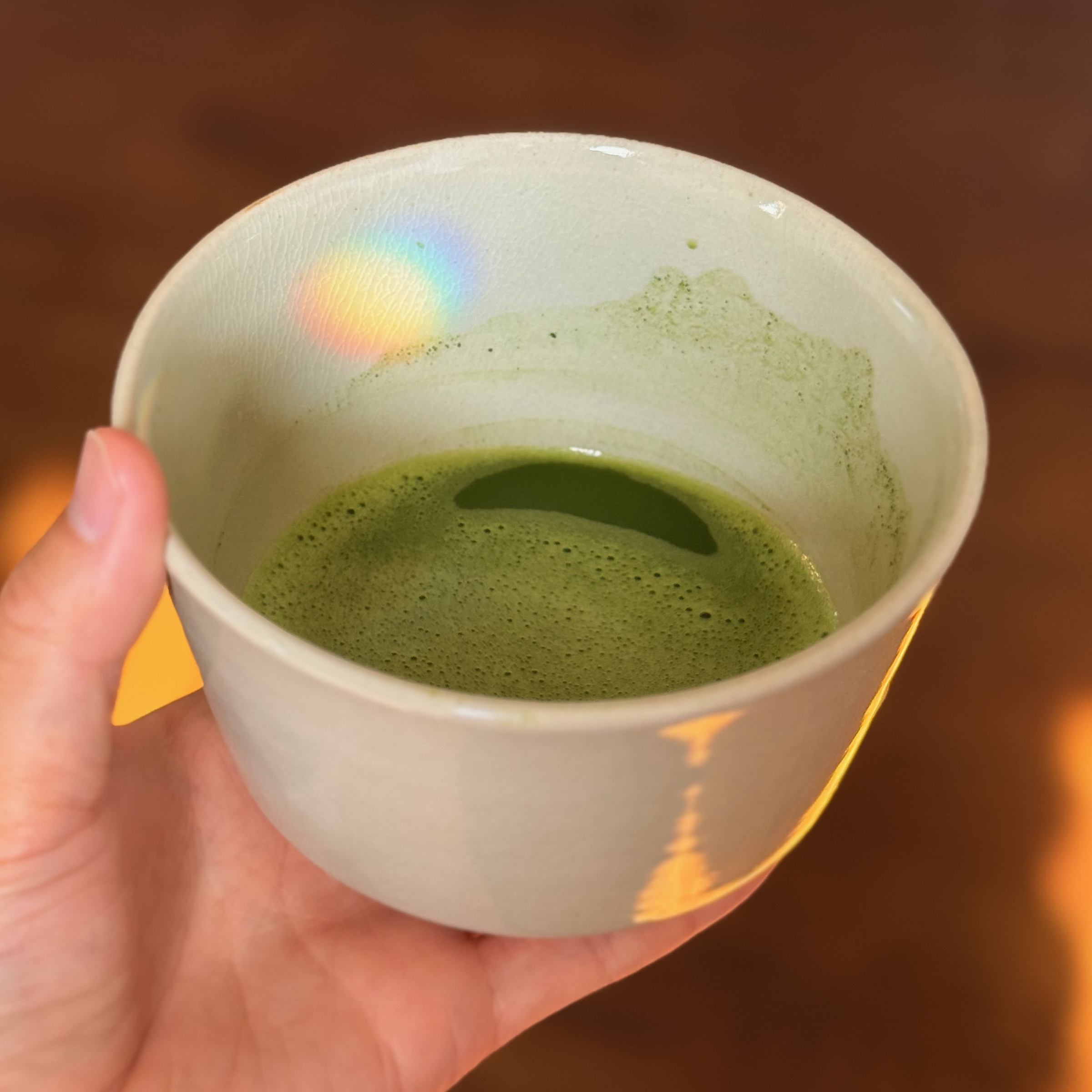 A bowl of matcha held in the hand, on a wooden floor at home